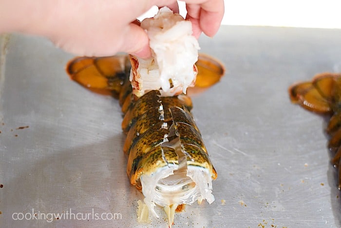 A hand lifting the lobster flesh out of the cut shell.