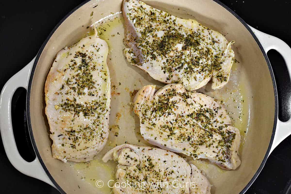 Browned chicken breast in a skillet with oil.