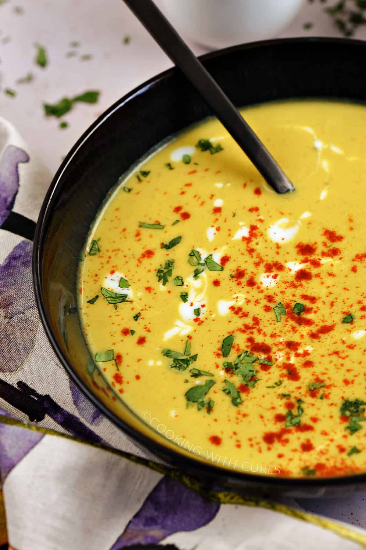 Butternut Squash Soup topped with chopped cilantro, kefir, and paprika in a dark bowl with a black spoon. 