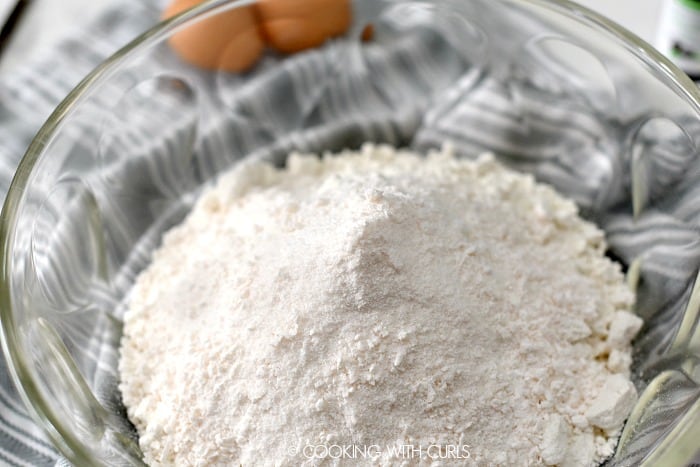 Cake and pudding mix in a large glass bowl with eggs in the background. 