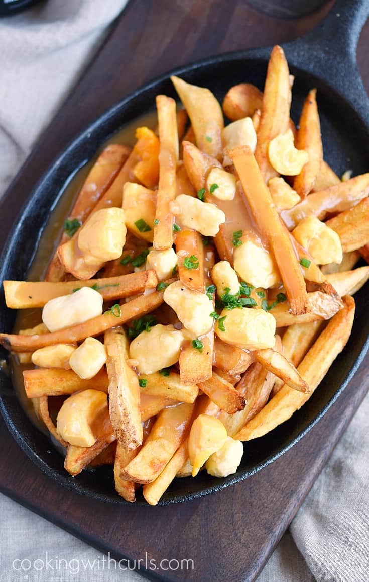 Looking down on French fries and cheese curds topped with brown gravy in an oval cast iron skillet.