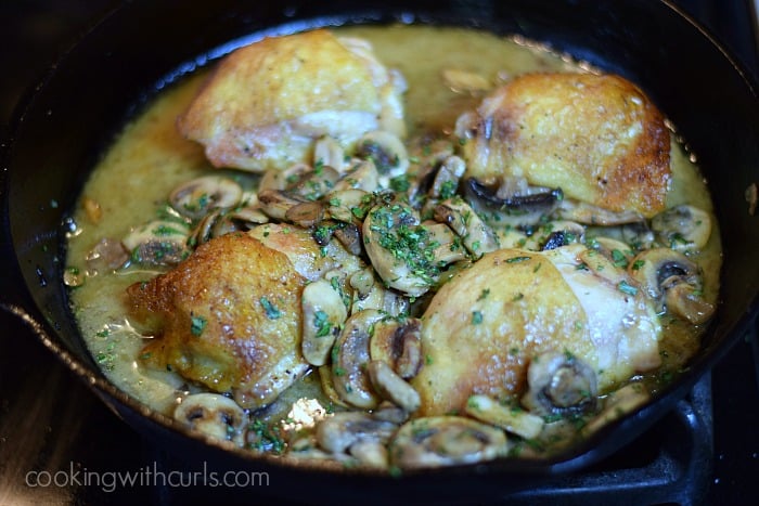 Four baked chicken thighs in a cast iron skillet with champagne, sliced mushrooms and chopped parsley.