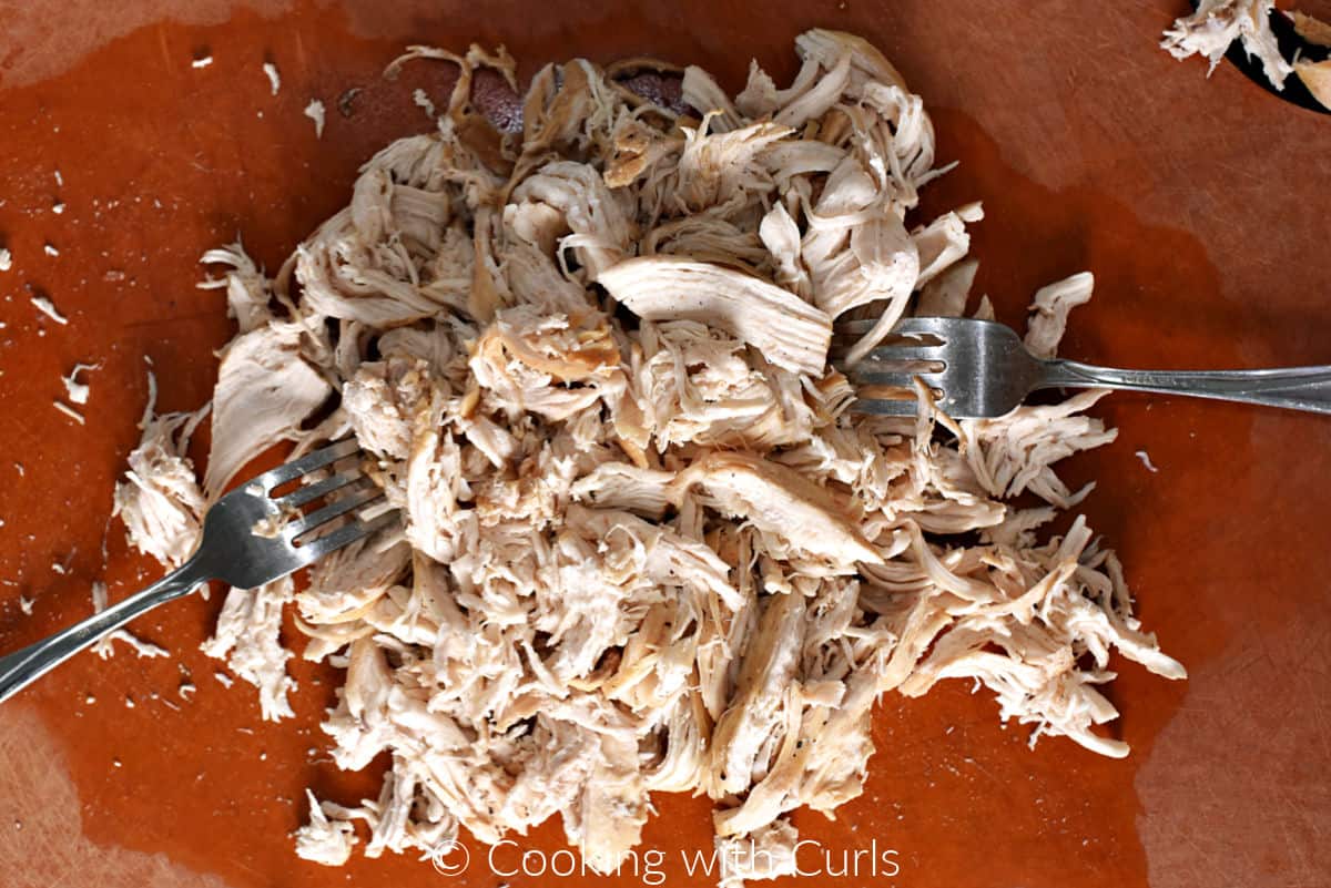 Chicken breasts shredded with two forks on a cutting board. 