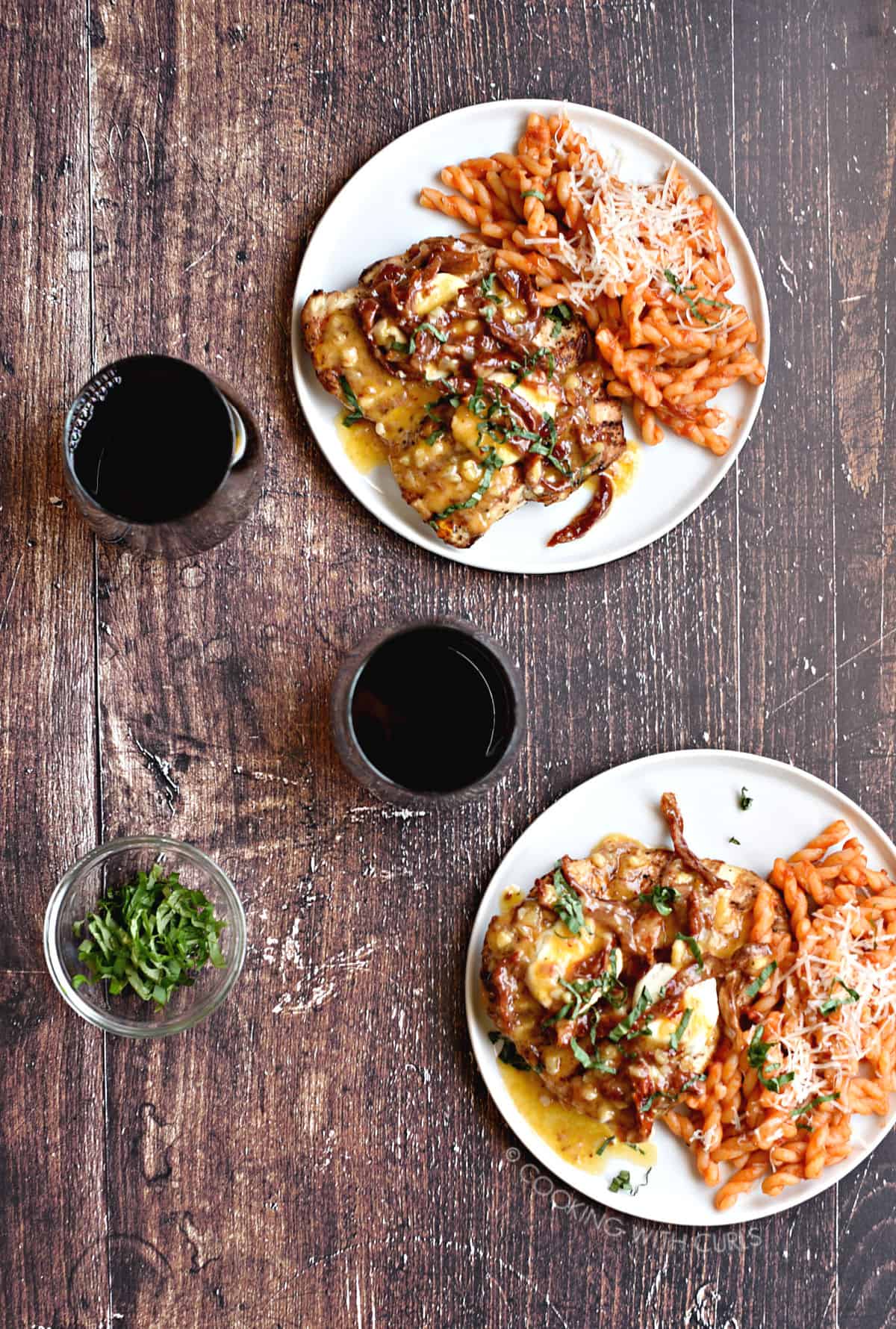 Looking down on two plates with Chicken Bryan, pasta and red wine. 