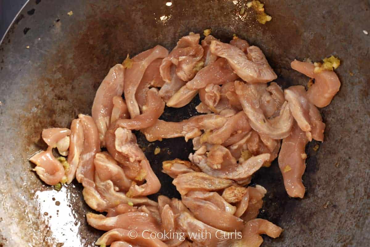 Chicken strips, oil, ginger, and garlic in a wok. 