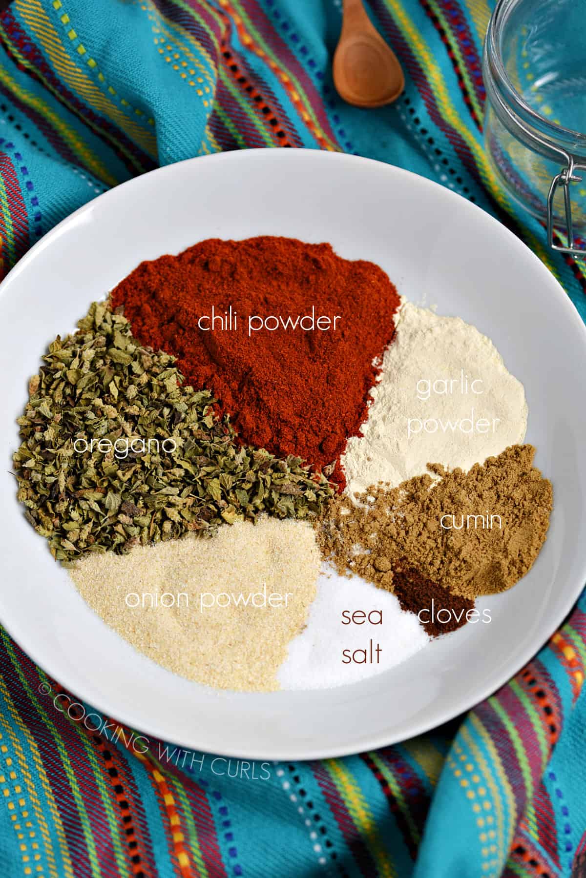 Chili powder, oregano, garlic powder, cumin, onion powder, cloves and sea salt in a white bowl. 