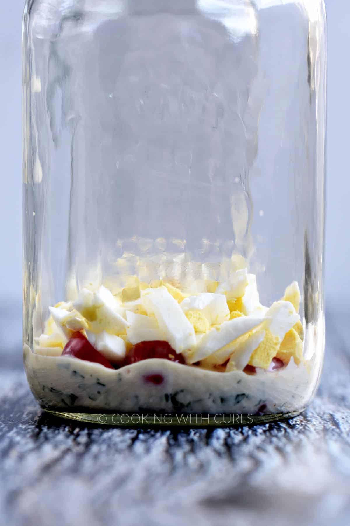 Chopped hardboiled eggs and tomatoes on ranch dressing in a Mason jar. 