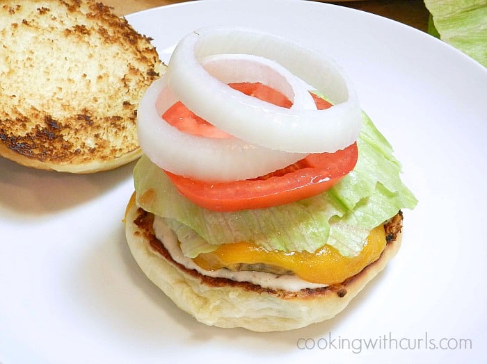 An open cheeseburger on a plate topped with lettuce, tomato, and onion slices.