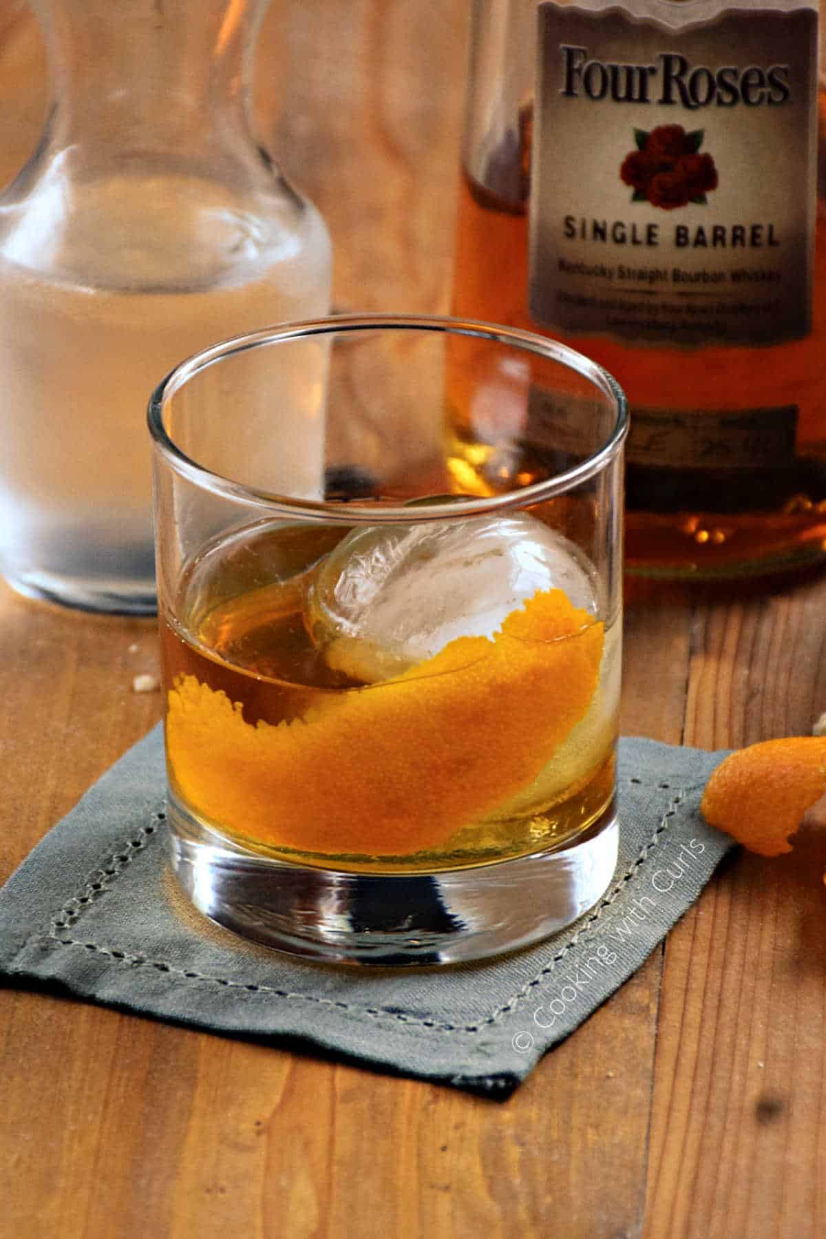 Bourbon cocktail with ice ball and orange twist in a rocks glass.