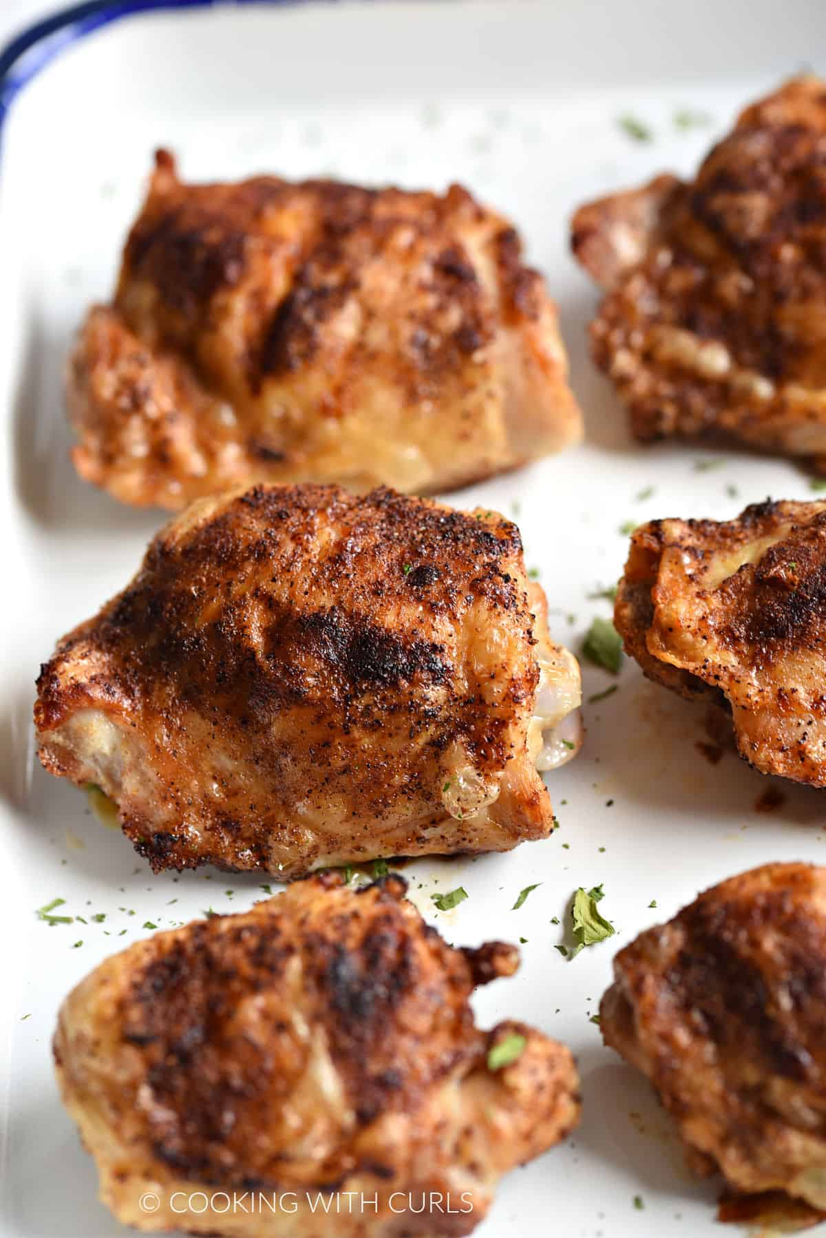 Close up image of six crispy chicken thighs on a white platter.