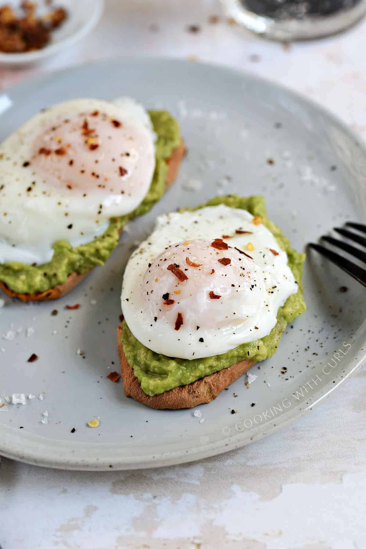 Close-up image of two poached eggs sprinkled with red pepper and salt flakes on avocado toast. 