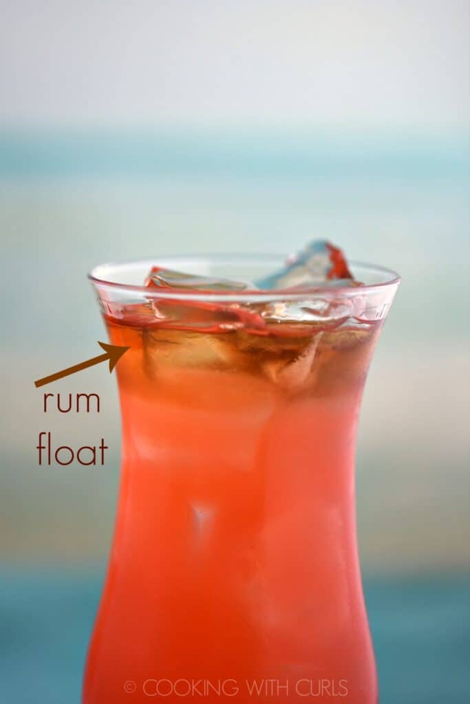 close up of pink cocktail with a dark rum float on top of the ice cubes.
