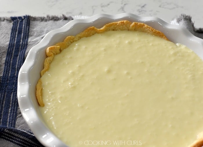 Coconut filling poured into the prepared pie crust in a white pie dish 