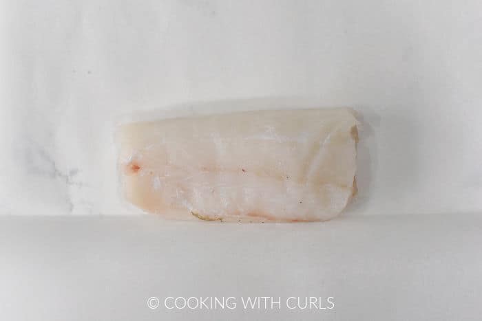 Cod filet on a sheet of parchment paper that is folded in half. 