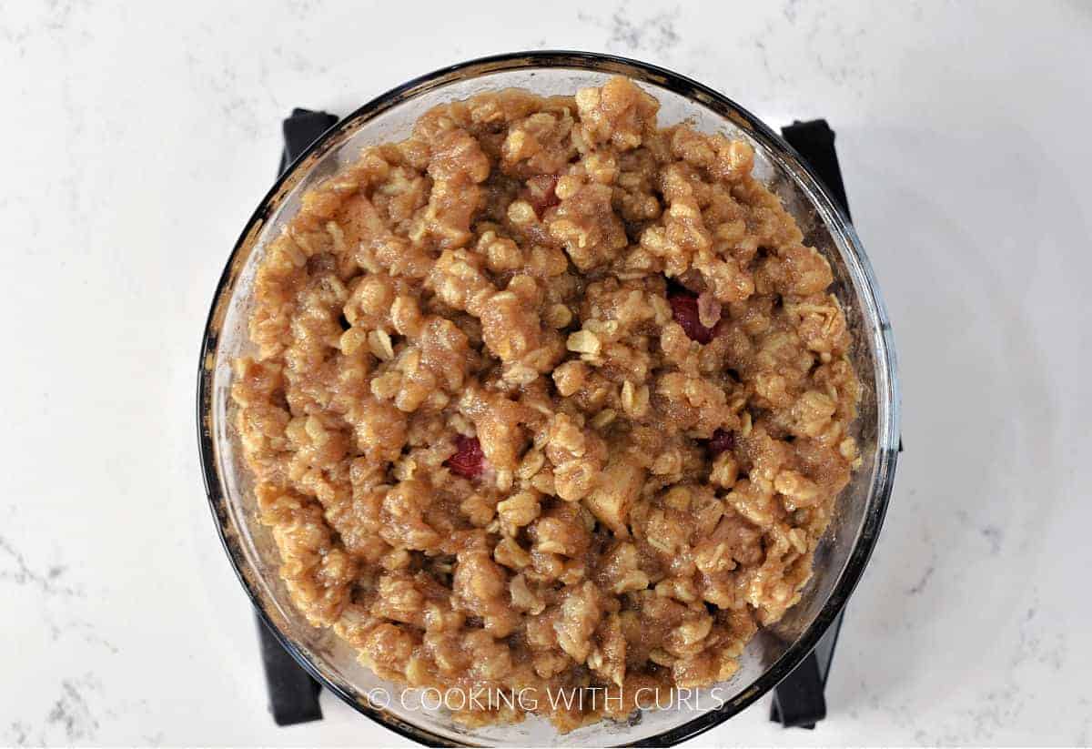 Cooked apple cranberry crisp in a small glass bowl sitting on a silicone trivet. 