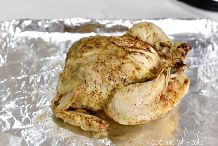 Cooked whole chicken on a foil lined baking sheet. 