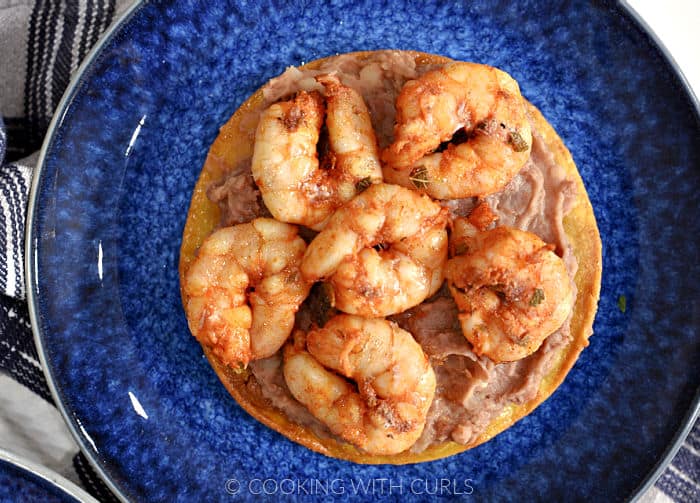 Corn tortilla topped with seasoned shrimp and refried beans on a blue plate. 