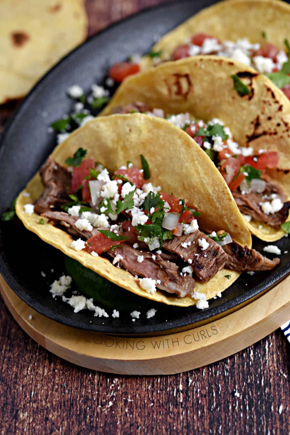 Corn tortillas filled with steak, diced tomatoes and onions sprinkled with queso crumbles and cilantro on a skillet. 