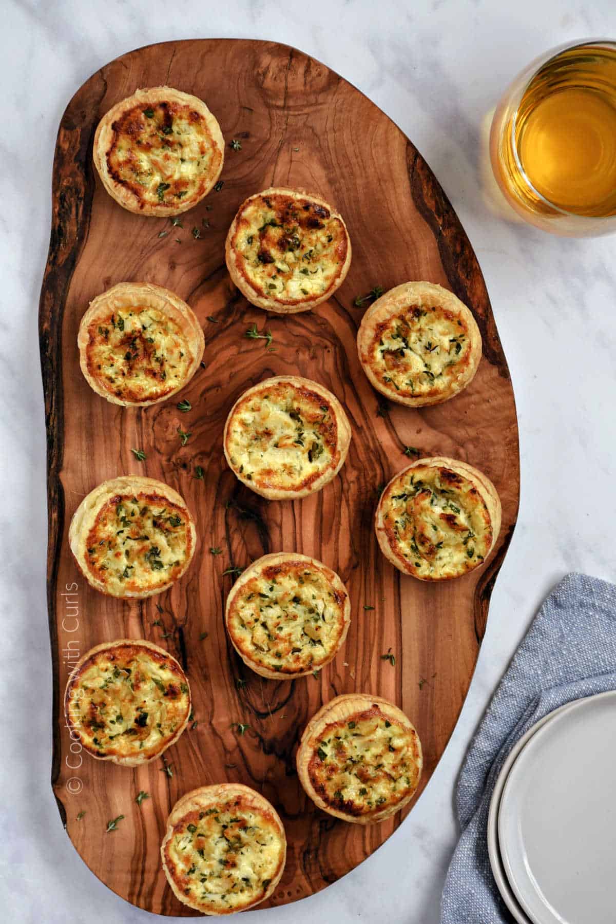 Eleven crab puff pastry tartlets on a wood board.