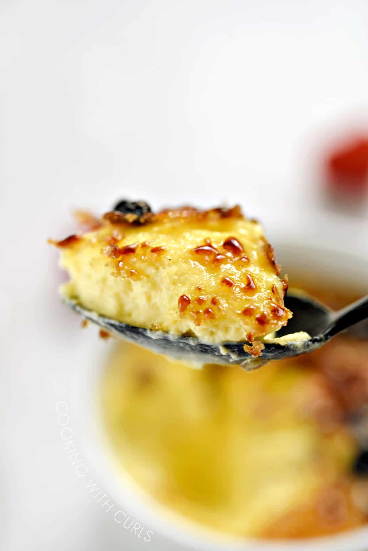 A bit of caramelized cream brulee on a spoon with the ramekin below.