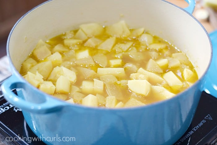 Cooked potato and parsnip chunks in broth inside a blue pot.