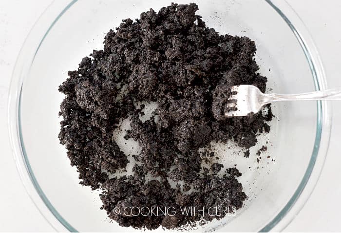 Crushed chocolate sandwich cookies mixed with melted butter in a glass bowl. 