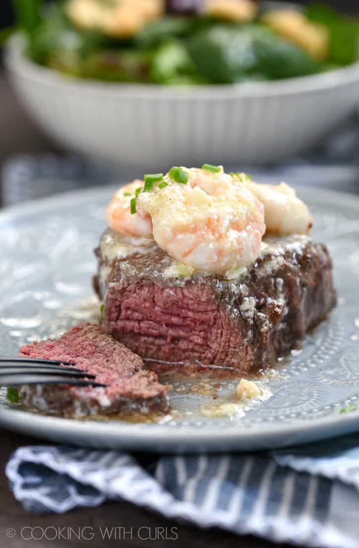 a cut filet mignon sitting on a gray plate topped with shrimp scampi