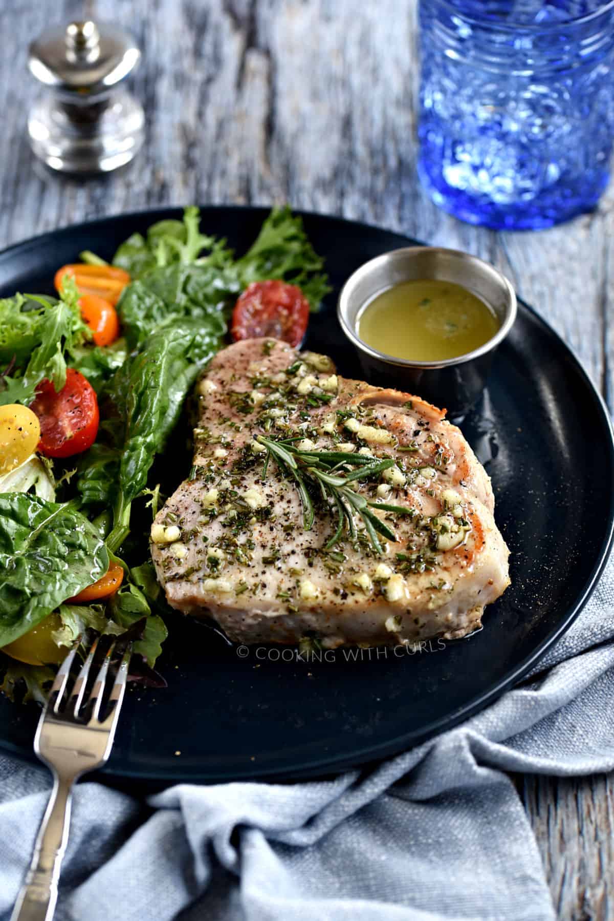 Thick, bone-in pork chop topped with garlic-rosemary butter with a green salad and cherry tomatoes on the side.