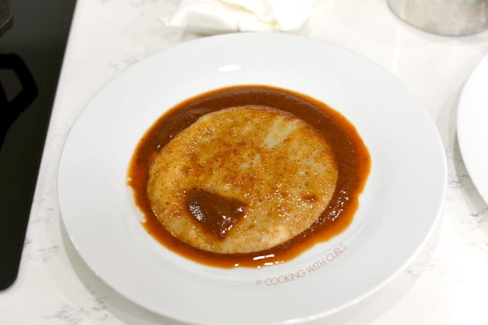 Fried tortilla coated in enchilada sauce on a plate.