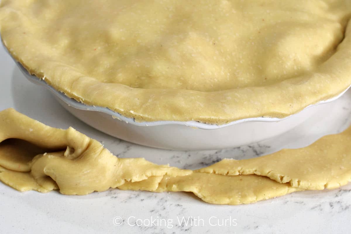 Double crust pie dough trimmed around the edge of a white pie plate. 