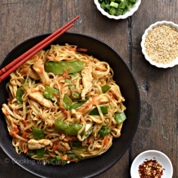 Looking down on chicken, noodles, snow peas, and shredded carrots in a large black bowl.