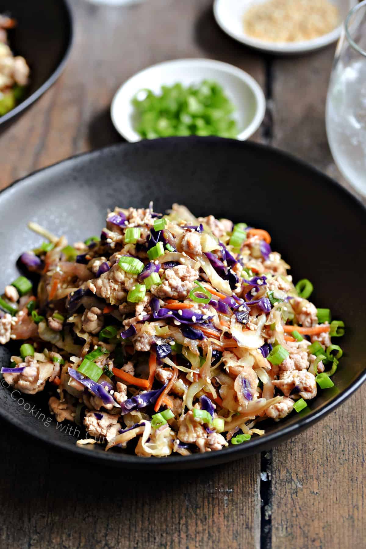 Egg roll in a bowl mixed together in a black bowl and topped with green onions.