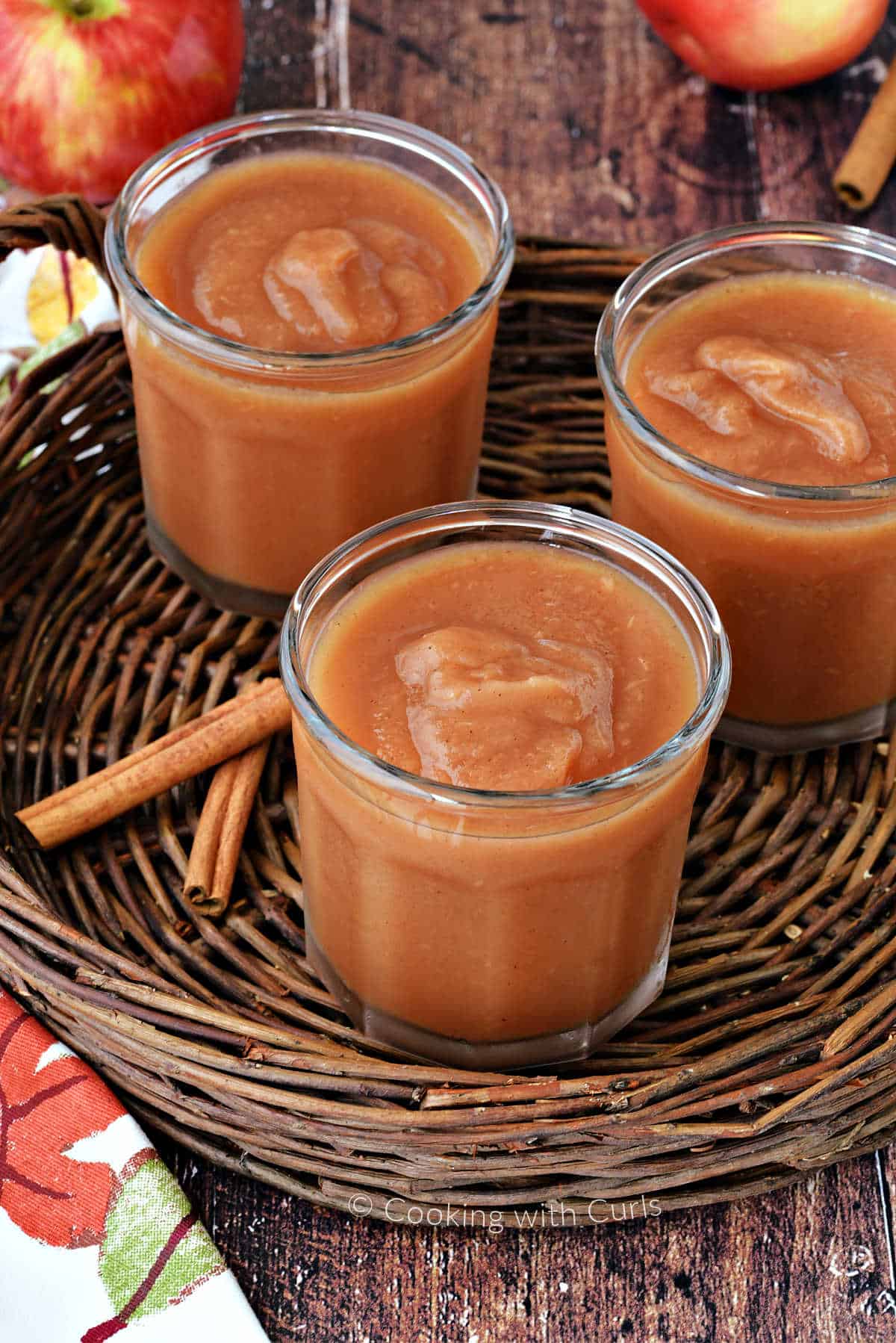 Three jars filled with apple butter on a wicker tray with cinnamon sticks and a fall napkin.