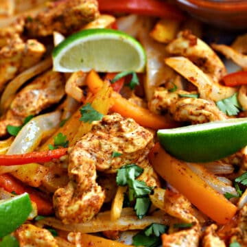 Strips of chicken, onion, red, orange and yellow bell peppers, and lime wedges with salsa in the upper right hand corner.