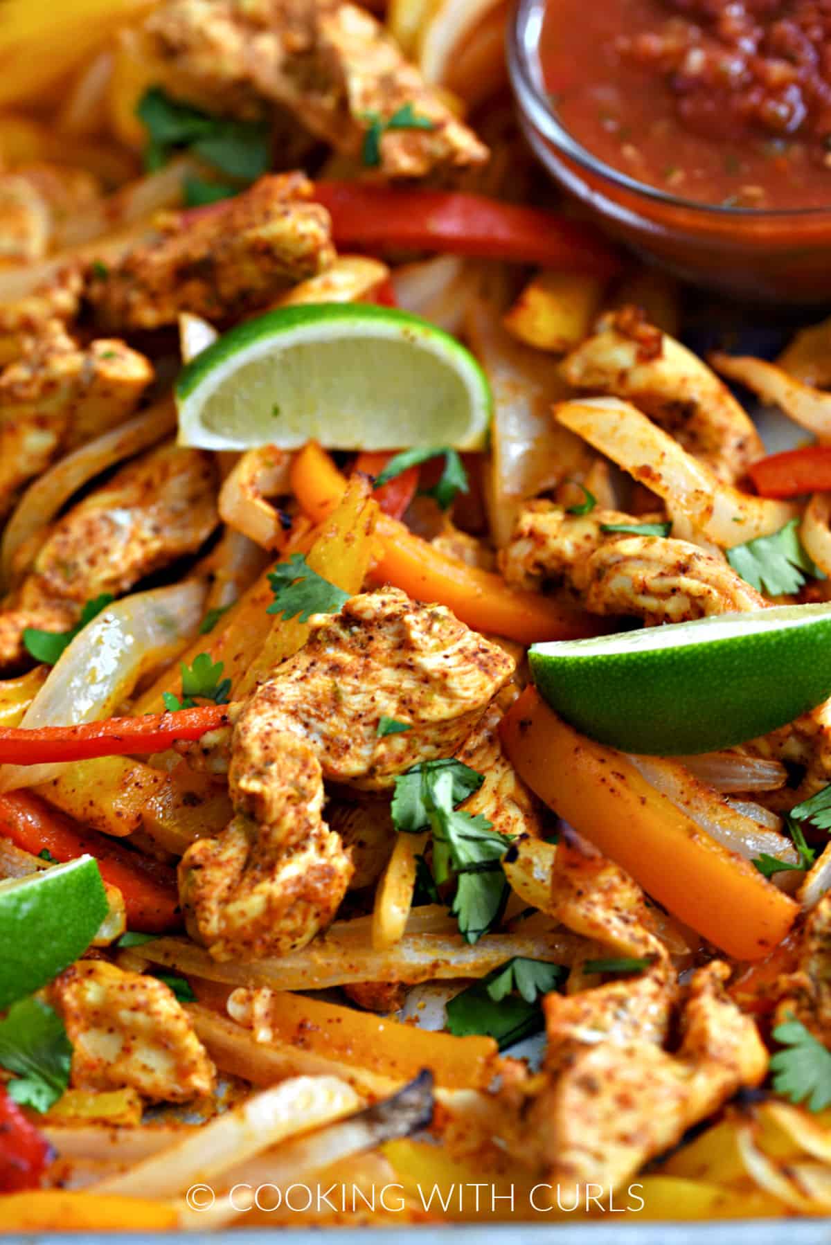 Strips of chicken, onion, red, orange and yellow bell peppers on a sheet pan. 