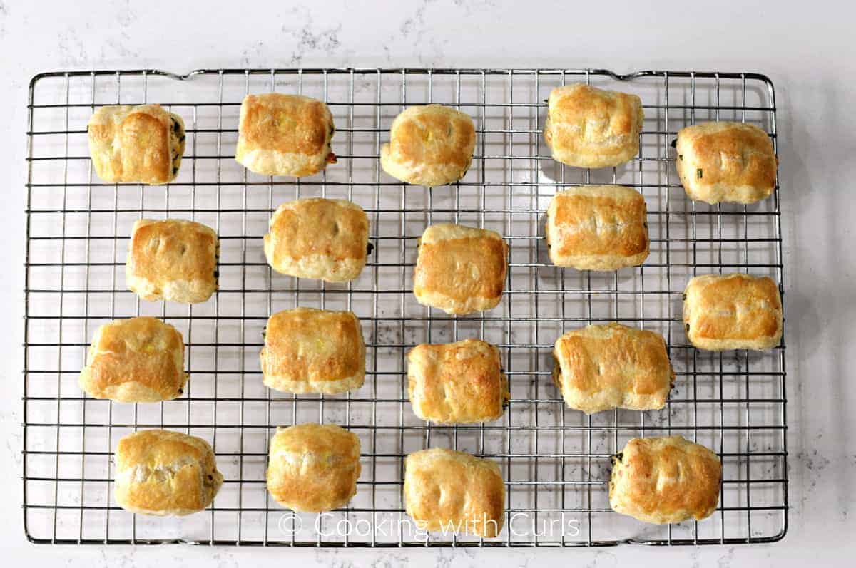 Eighteen baked puff pastry chicken sausage rolls on a wire cooling rack. 