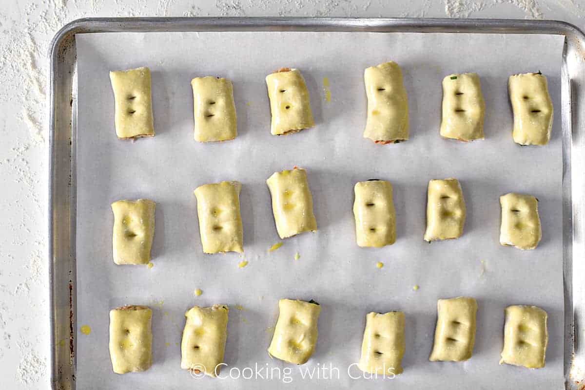 Eighteen raw chicken sausage rolls on a parchment lined baking sheet brushed with egg wash. 