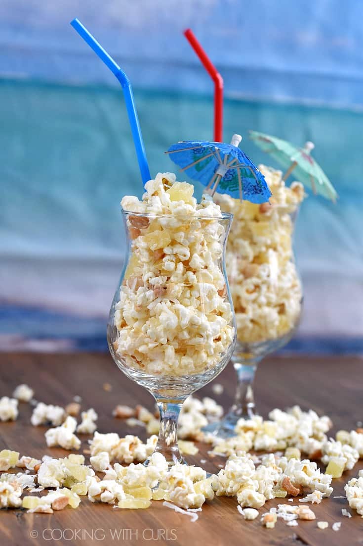 Two cocktail glasses filled with Pina Colada Popcorn with straws and paper umbrellas