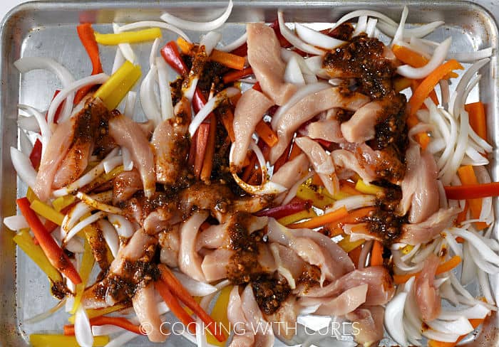 Fajita marinade poured over strips of chicken, onion, and bell peppers on a sheet pan. 