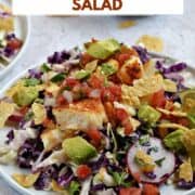 Seasoned cod on top of shredded cabbage with chopped tomatoes and avocado and crushed tortilla chips on a dinner plate with title graphic across the top.