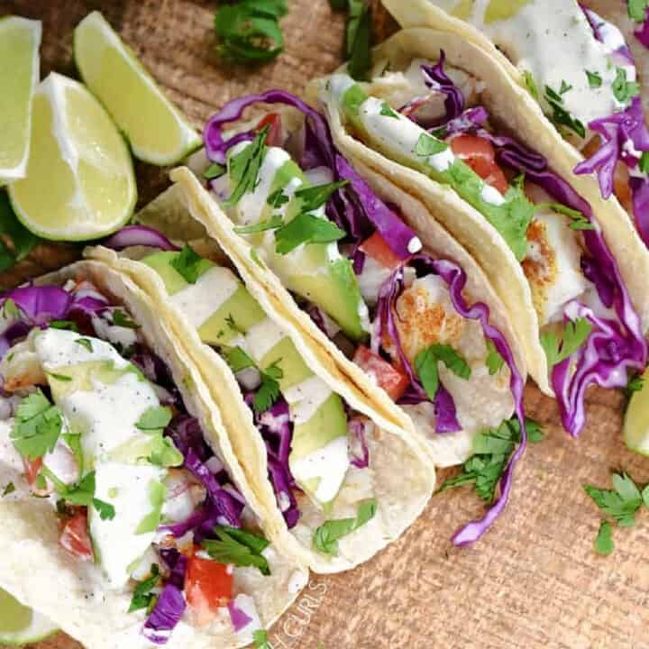 Looking down on three fish tacos with crema, cilantro, and cabbage on a wood board.