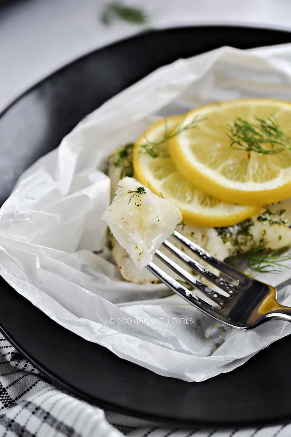 Flaky cod on a fork resting next to a lemon topped filet. 