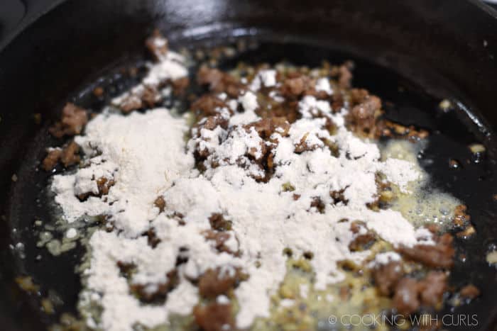 flour sprinkled over cooked sausage and onions in a cast iron skillet. 