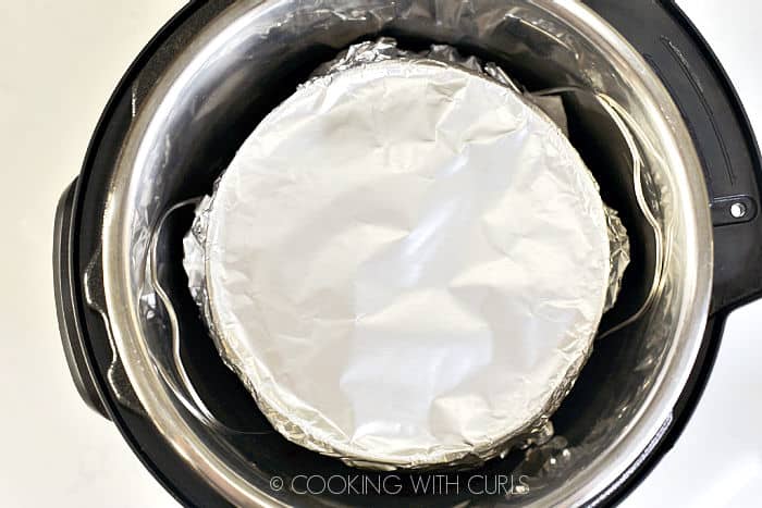 Foil wrapped cheesecake sitting on a trivet inside the pressure cooker. 