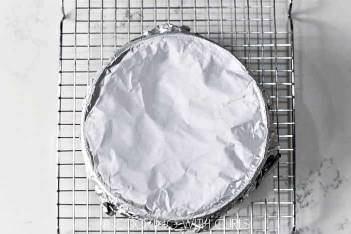 Foiled covered cheesecake on a wire cooling rack.