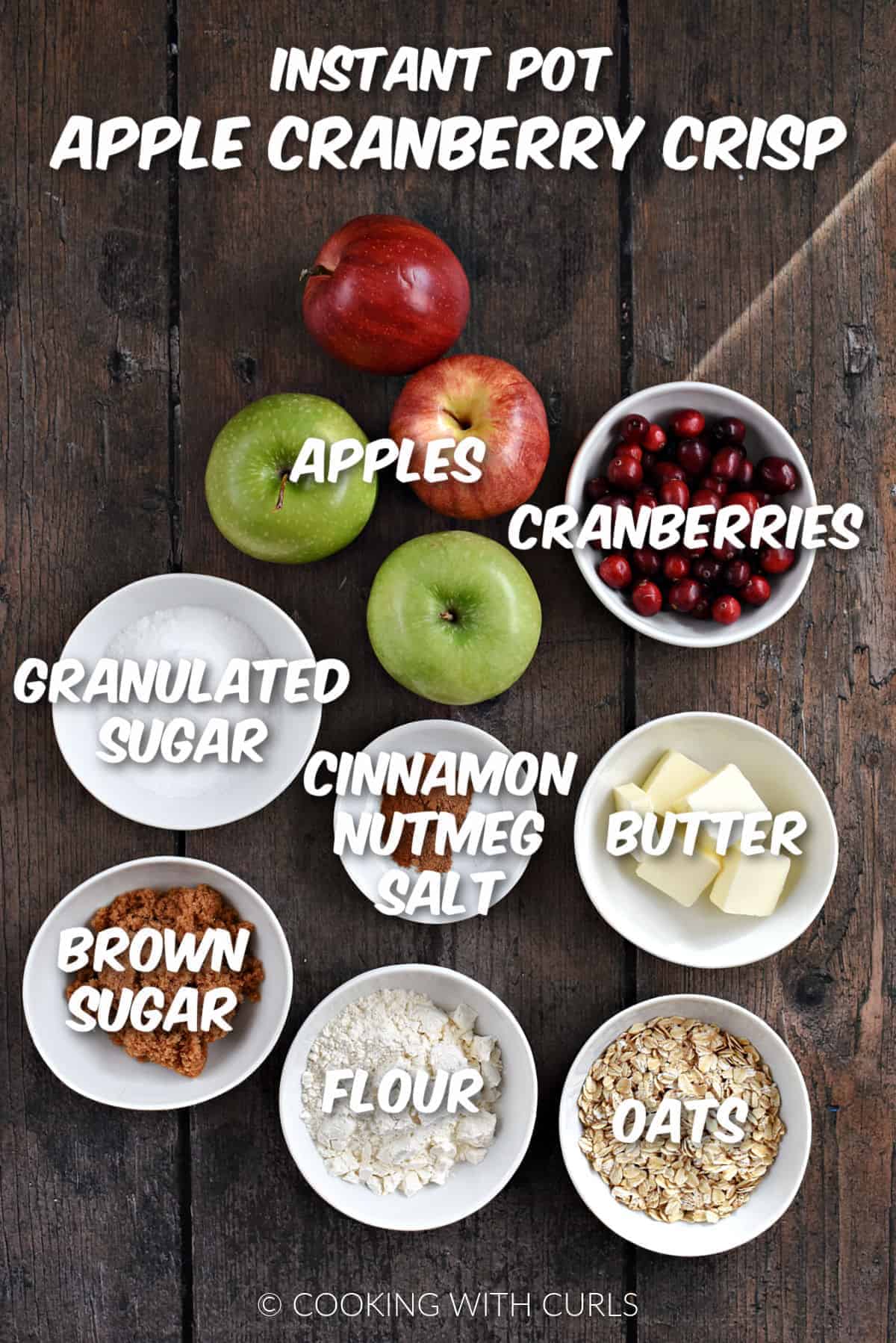 Four apples, cranberries, sugars, butter, flour, oats and seasonings in white bowls. 