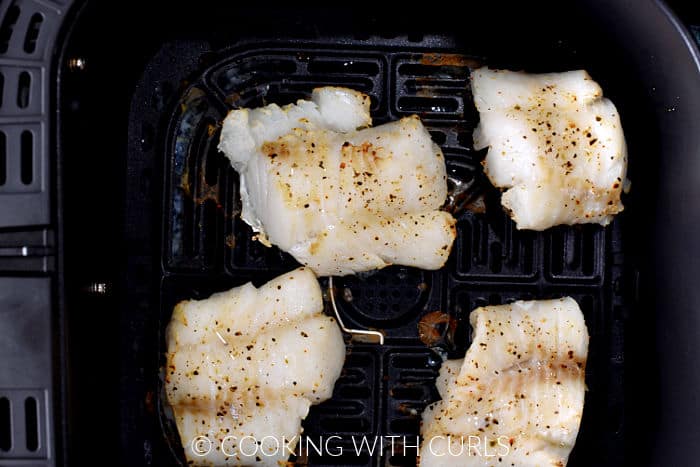 Four baked cod filets in an air fryer basket. 