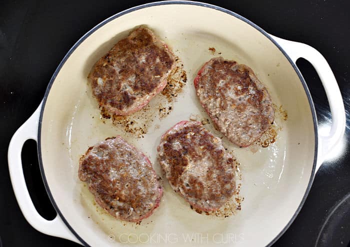 Four browned salisbury steak patties in a cast iron skillet. 