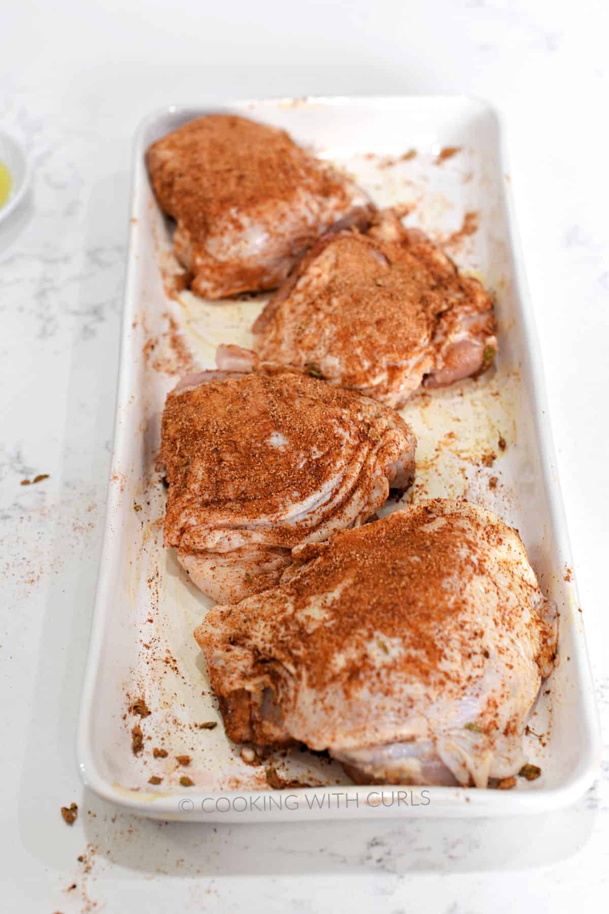 Four chicken thighs covered in Mexican seasoning on a white platter.