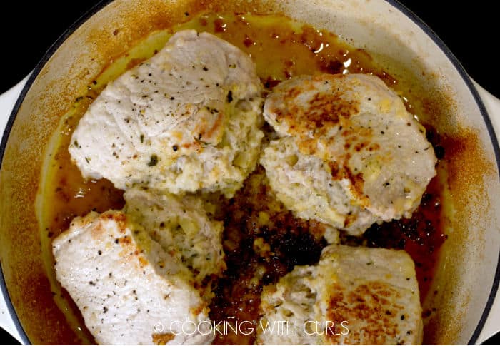 Four cooked, stuffed pork chops in a white skillet. 